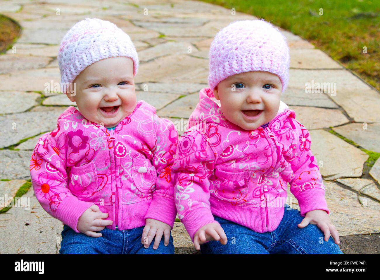 Dos camas de bebé niña sentada sobre una piedra pasarela vistiendo sudaderas y rosa beanies. Foto de stock