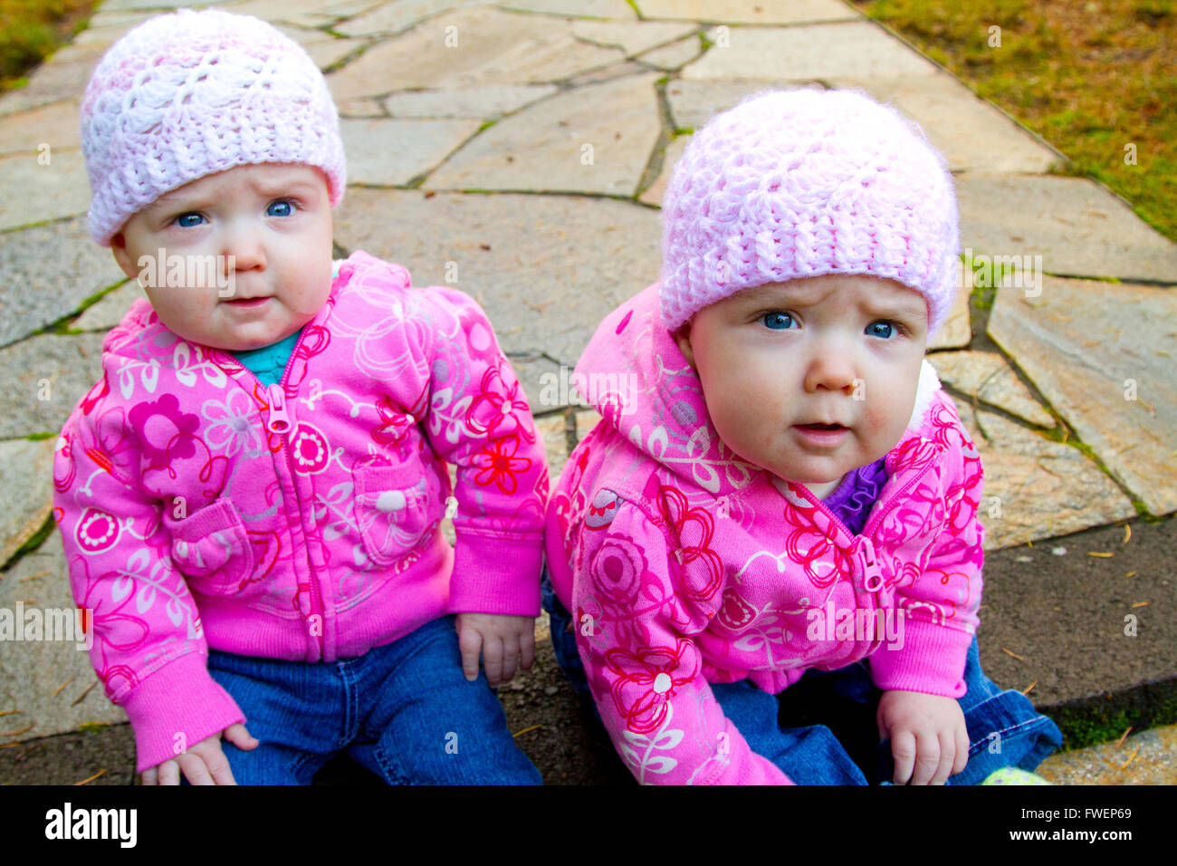 Dos camas de bebé niña sentada sobre una piedra pasarela vistiendo sudaderas y rosa beanies. Foto de stock