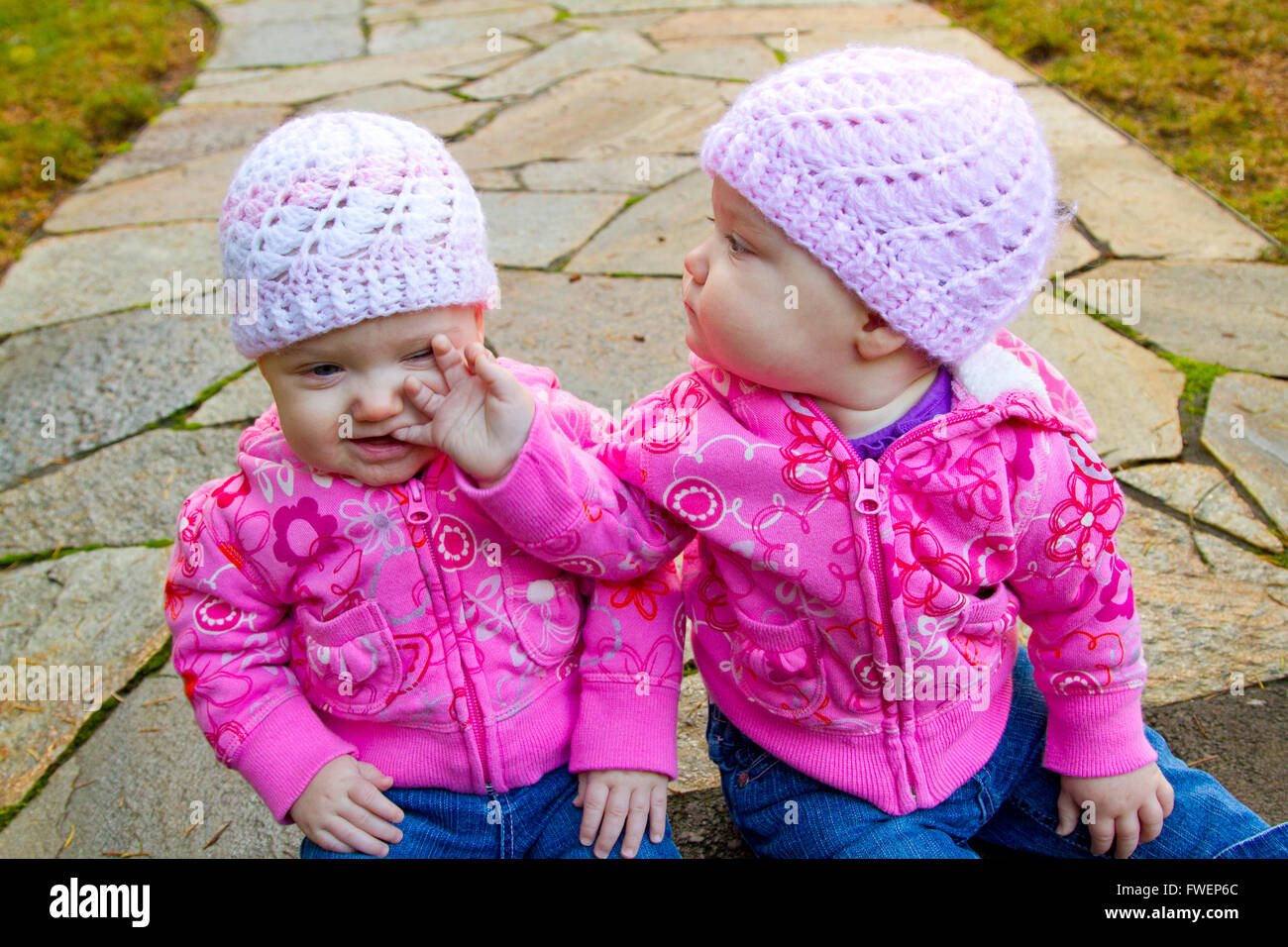 Dos camas de bebé niña sentada sobre una piedra pasarela vistiendo sudaderas y rosa beanies. Foto de stock