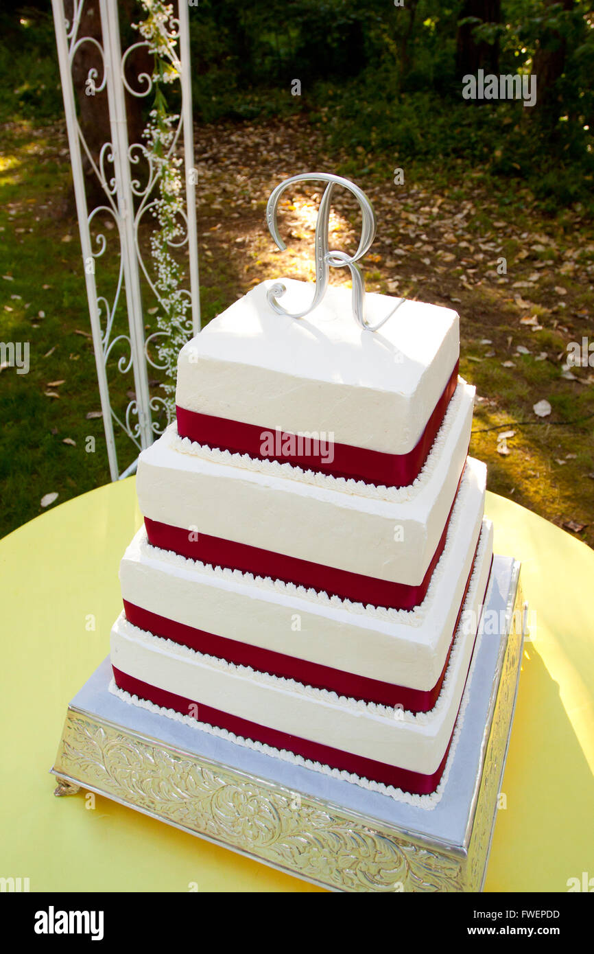 Un cuadrado rojo y blanco pastel de boda con múltiples niveles y la letra R  en la parte superior se encuentra fuera sobre una tabla de color amarillo  para una boda rec