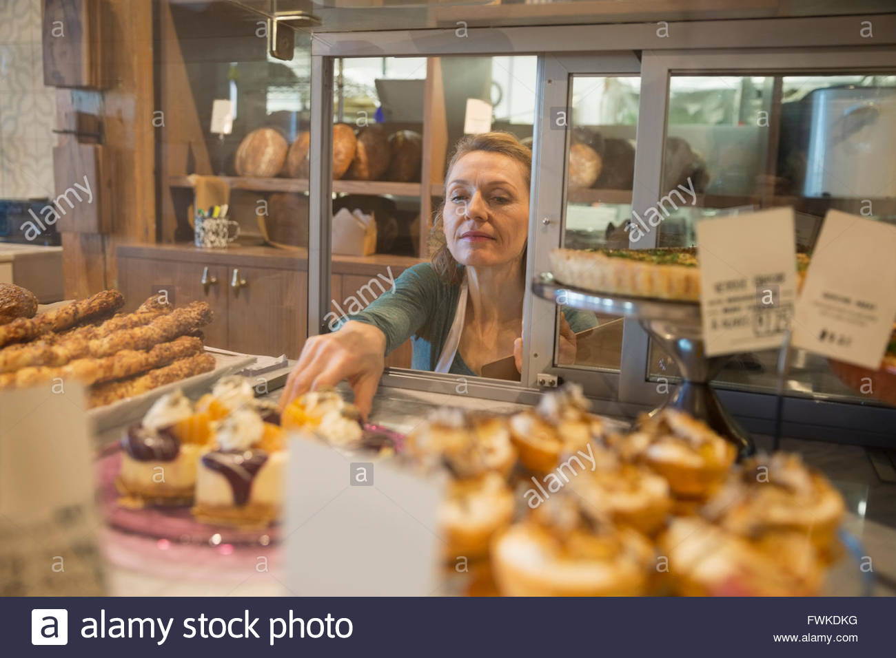 Propietario de panadería alcanzando para pastelería en vitrina Foto de stock