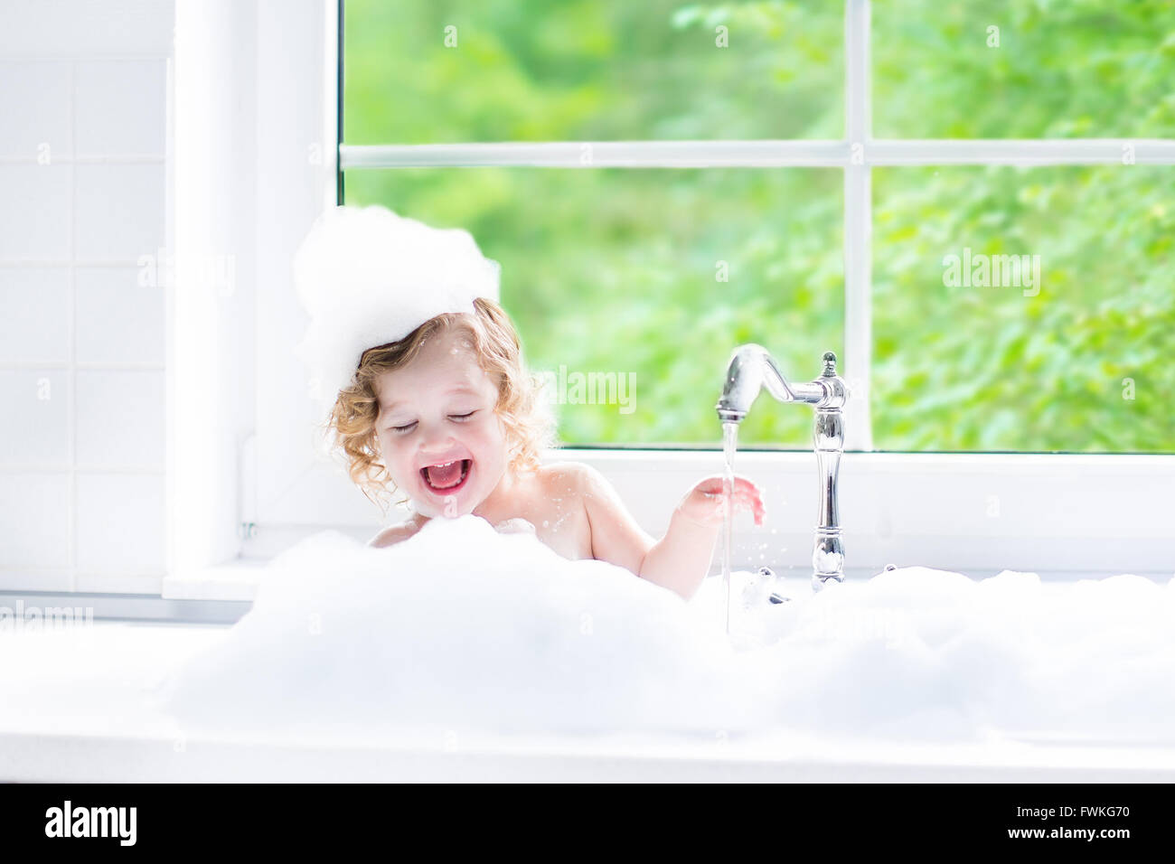 Niño de tomar un baño. Pequeño bebé en una tina de lavar el cabello con  champú y jabón. Niños jugando con la espuma y las salpicaduras de agua  Fotografía de stock -