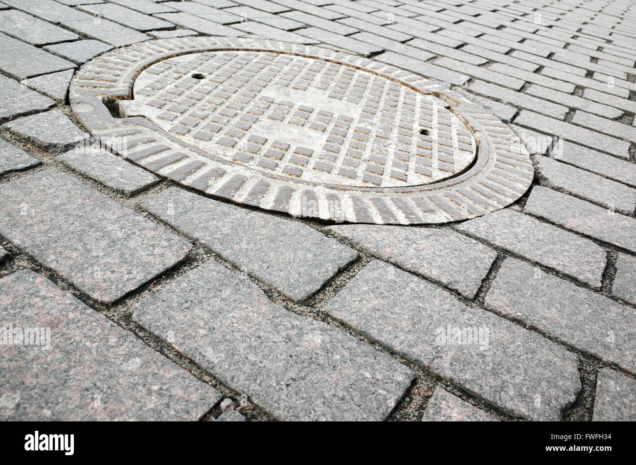 Rusted redonda eclosionan en pavimento de adoquines de alcantarillado