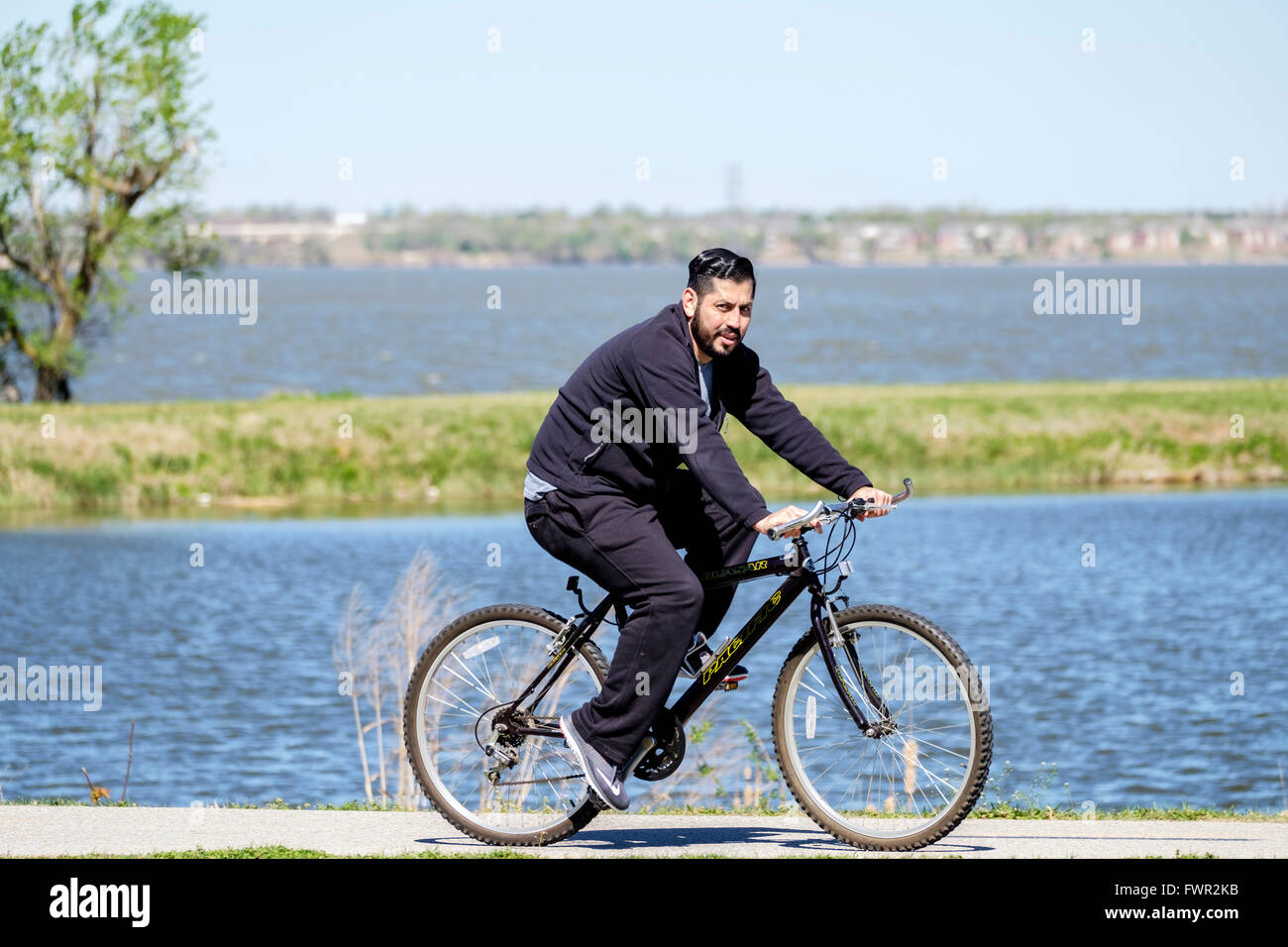 Un hombre hispano de bicicletas para ejercer sobre los senderos junto al río del norte de Canadá y el lago Overholser, Oklahoma City, EE.UU. Foto de stock