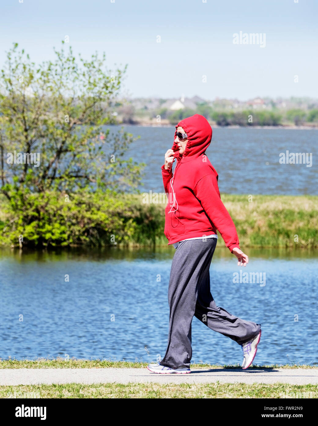 Una mujer en una hoodie camina sobre el ejercicio senderos en lago Overholser en Oklahoma City, Oklahoma, Estados Unidos, durante un fresco viento de primavera. Foto de stock