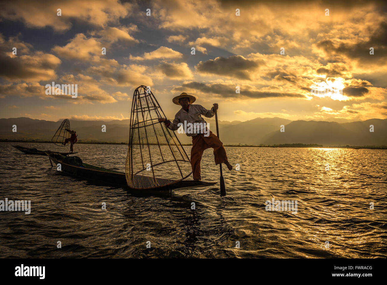 Dos pescadores pescan en un tradicional barco de bambú con una red artesanal al amanecer. Foto de stock