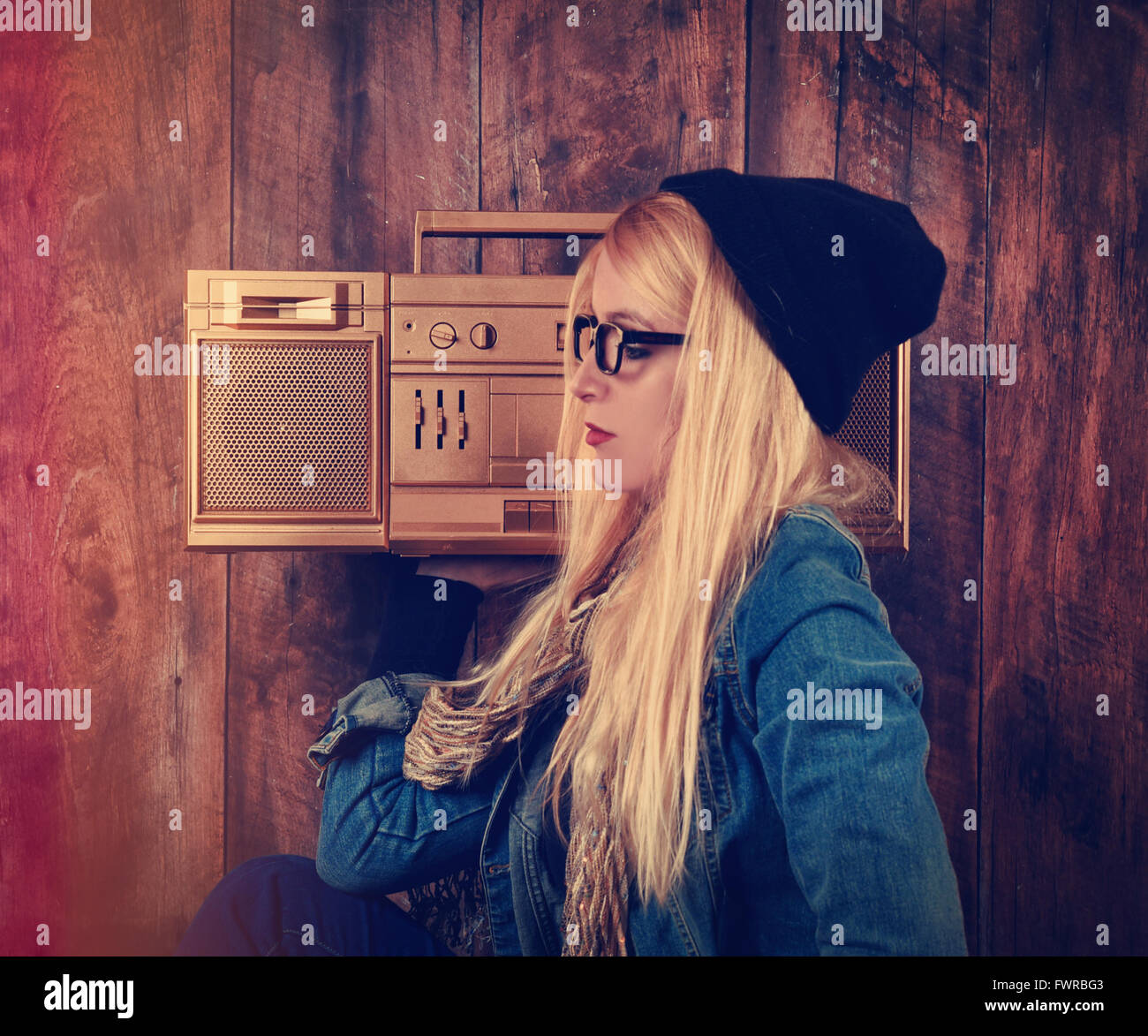 Un hipster chica con gafas es escuchar una vendimia oro boombox radio con un altavoz para un concepto de entretenimiento musical Foto de stock