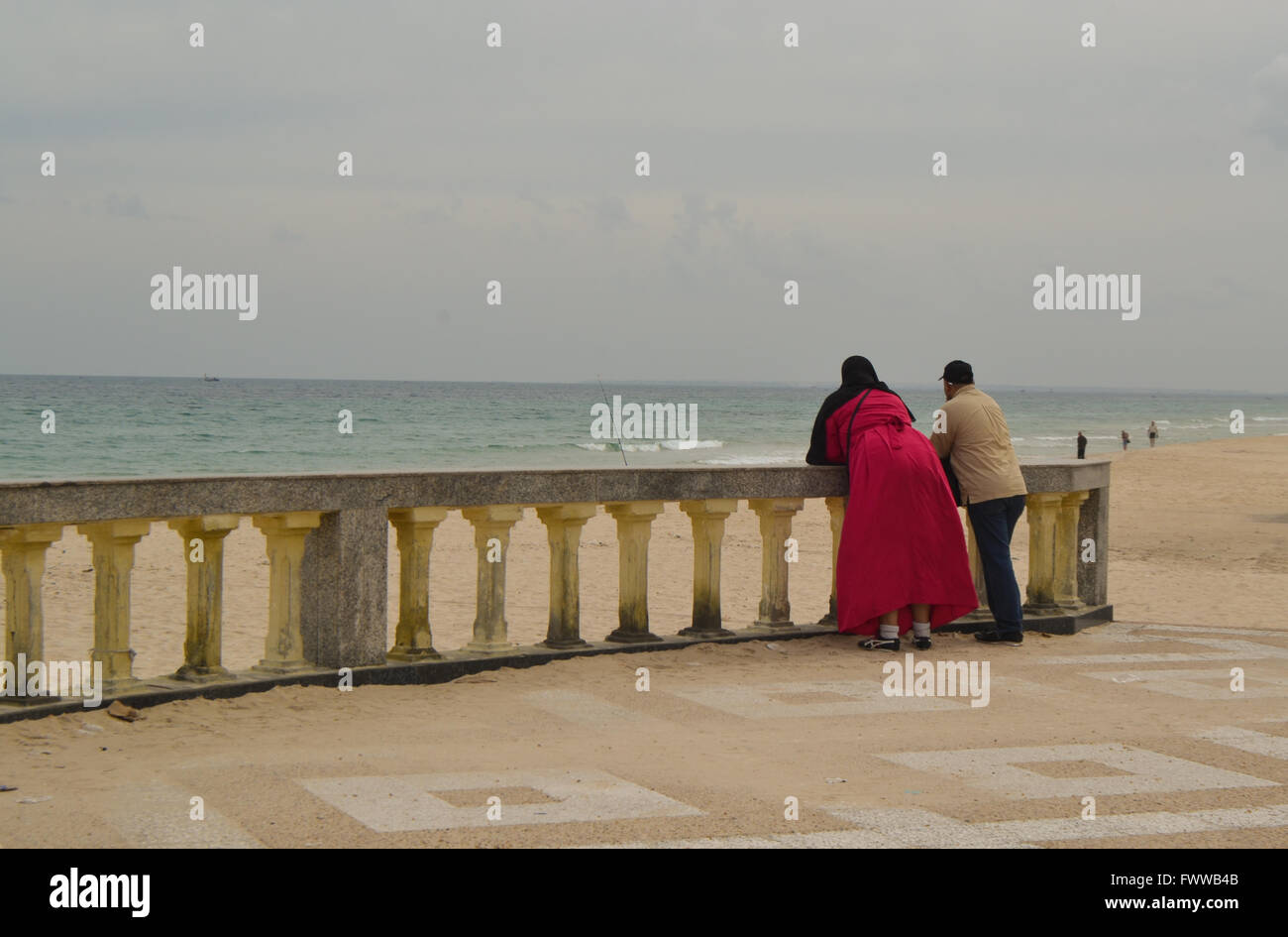 Pareja de musulmanes en la playa . La mujer está vestida de rojo burka. El mar está en calma. Foto de stock