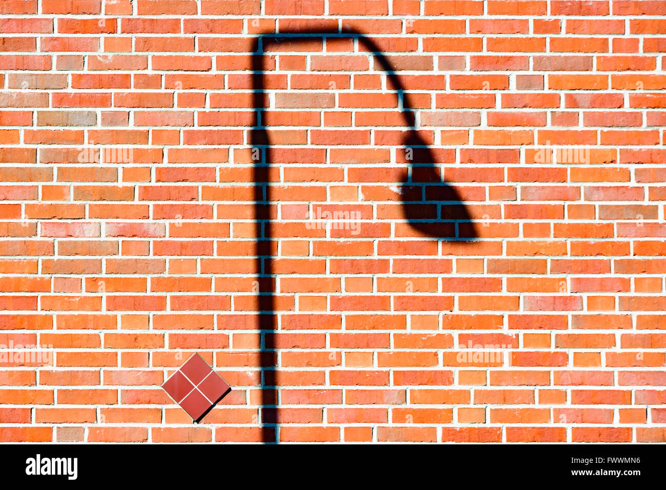 Farola oscura sombra que cae sobre una pared de ladrillo rojo. Foto de stock