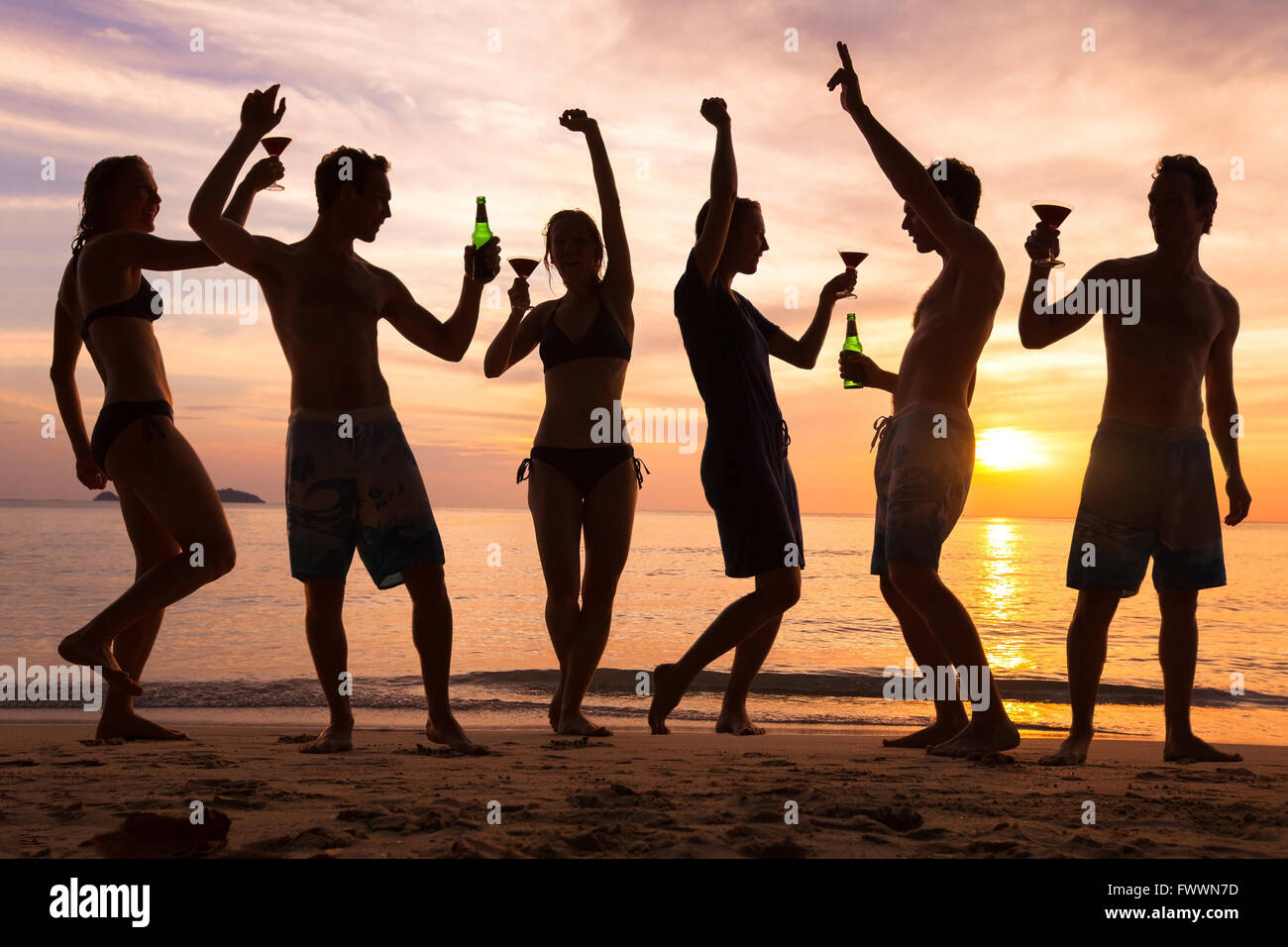 Fiesta en la playa, un grupo de jóvenes bailando, amigos bebiendo cerveza y cócteles al atardecer Foto de stock