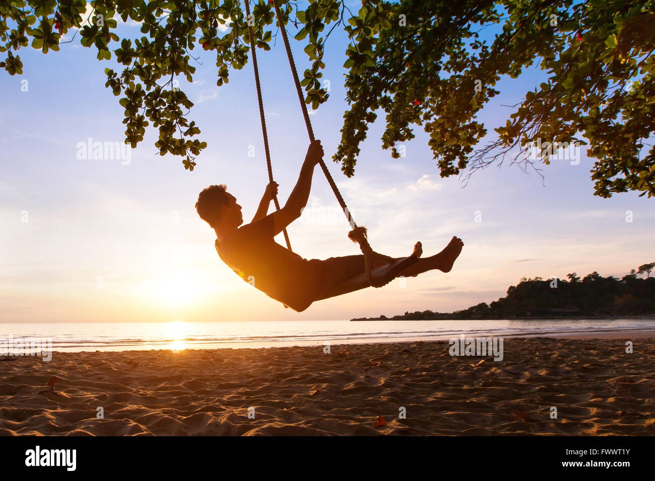 Swing en un paraíso tropical en la playa al atardecer, personas felices disfrutando del verano Foto de stock
