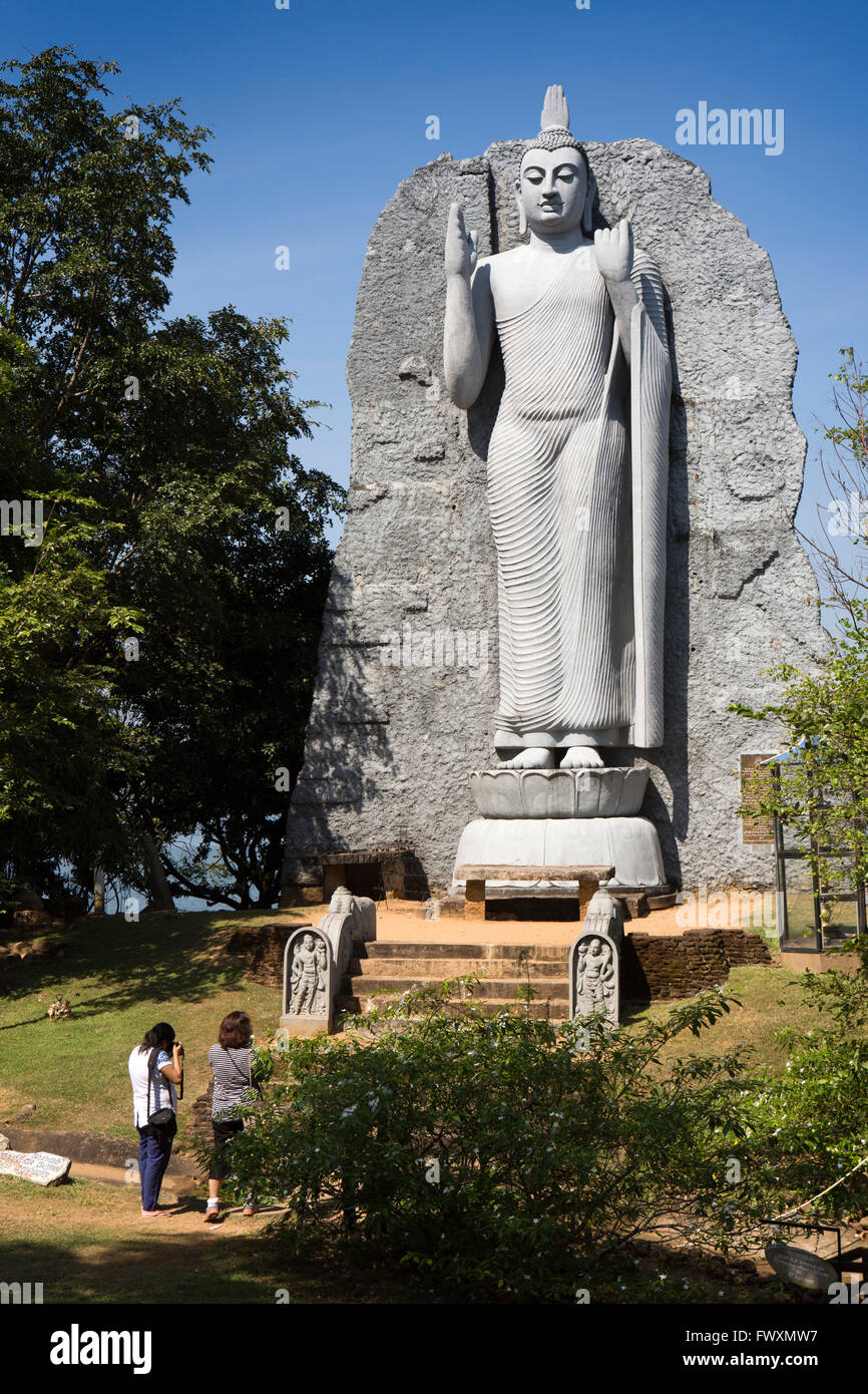 Sri Lanka, Minneriya, los visitantes al gran Buda de pie junto al lago Wewa Minneriya Foto de stock