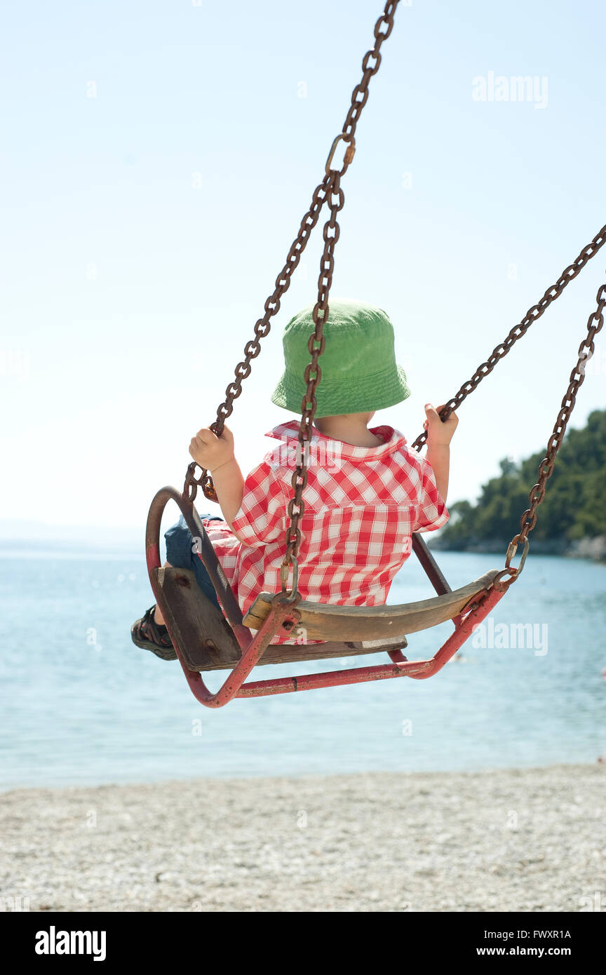 Grecia, Skopolos, Boy (4-5) en verde sombrero para el sol sentado en swing Foto de stock