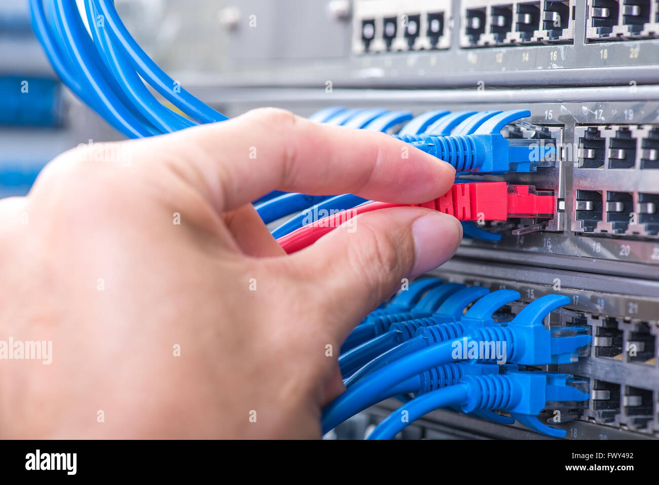 Hombre trabajando en la sala de servidores de red con cubo de fibra óptica para las comunicaciones digitales e internet Foto de stock