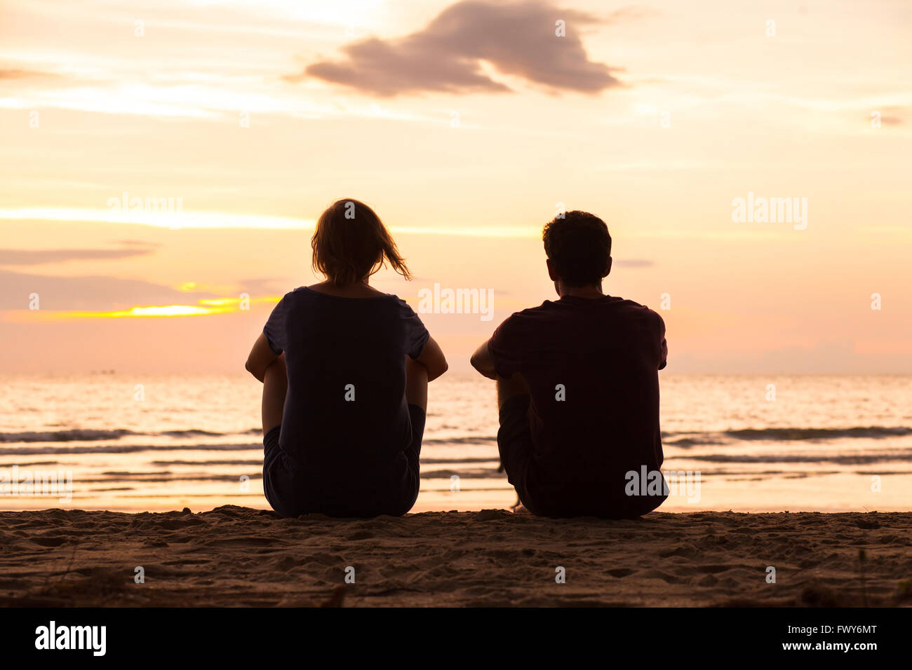 Amigos sentados juntos en la playa y observar el atardecer, concepto de amistad Foto de stock