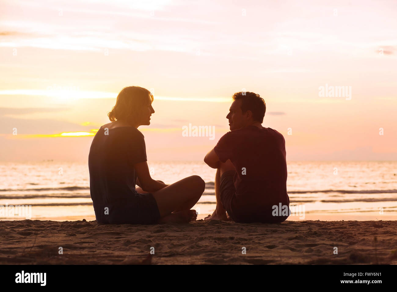 El hombre y la mujer en la playa al atardecer, pareja joven hablando cerca del mar, citas o concepto de amistad Foto de stock