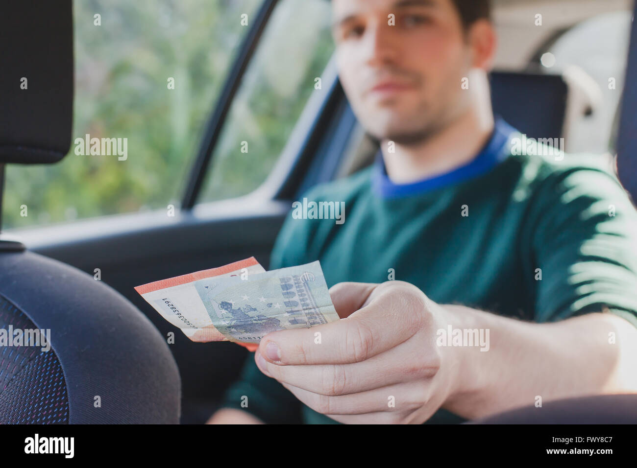 Pagar en efectivo en taxi, el acercamiento de la mano del pasajero dando dinero al conductor en el coche Foto de stock