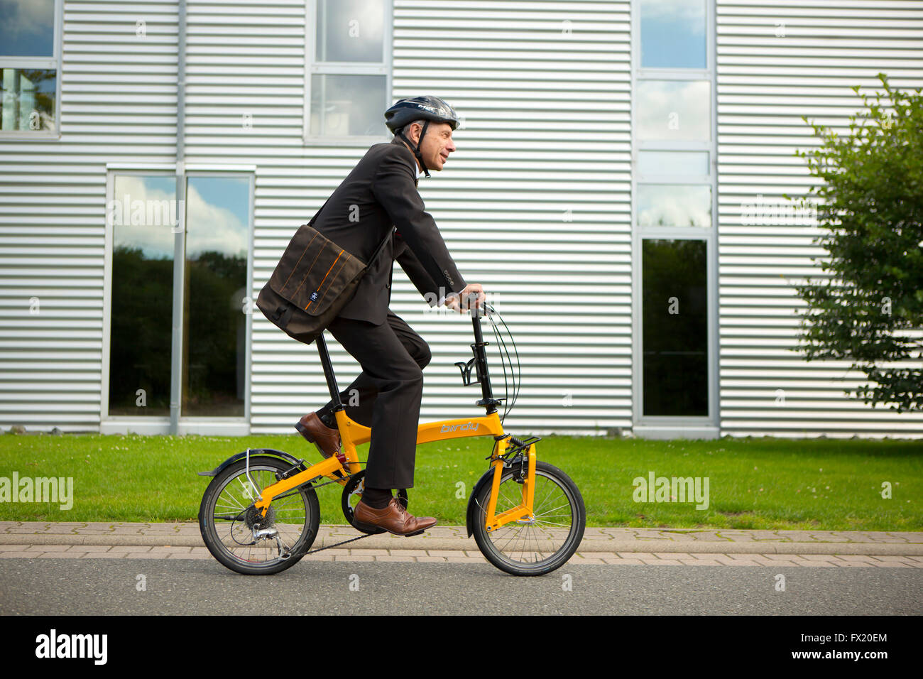 Empresario con casco montando una bicicleta plegable para trabajar Foto de stock