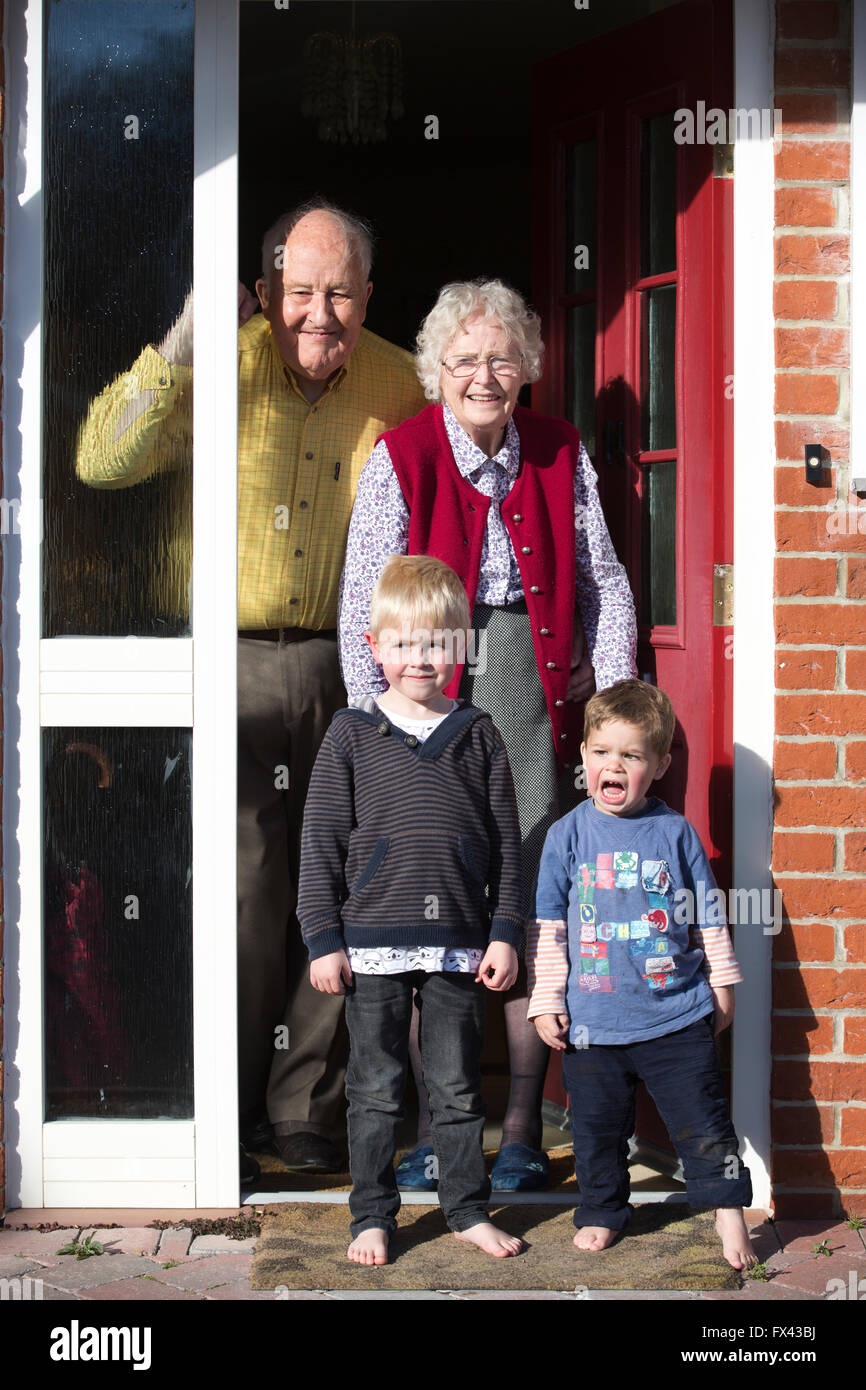 Los jubilados (en sus 80's) con sus nietos, en la puerta de su casa privada, Inglaterra, Reino Unido. Foto de stock