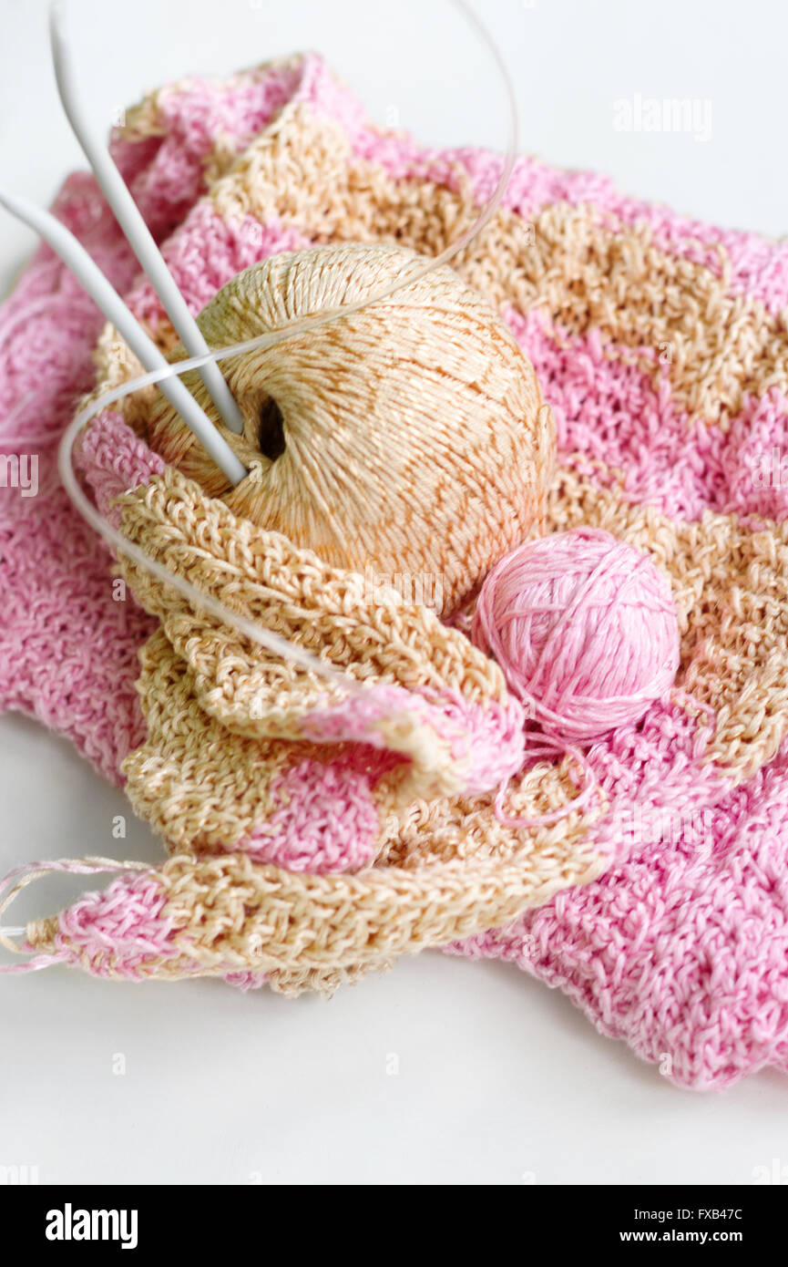 Preciosa bufanda de punto de rayas, agujas de tejer y dos bolas de hilo  sobre una tabla en blanco. Hilo es el rosa y el beige Fotografía de stock -  Alamy
