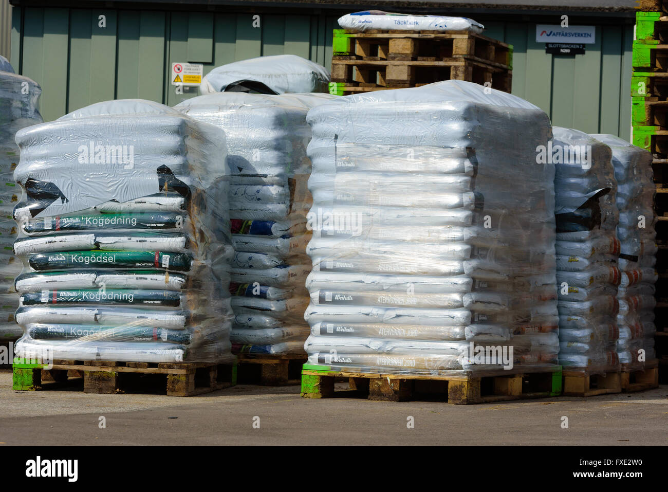 Lyckeby, Suecia, 7 de abril de 2016: palets de plástico envuelto el suelo y las bolsas de fertilizantes almacena detrás de una tienda en el área pública. Foto de stock