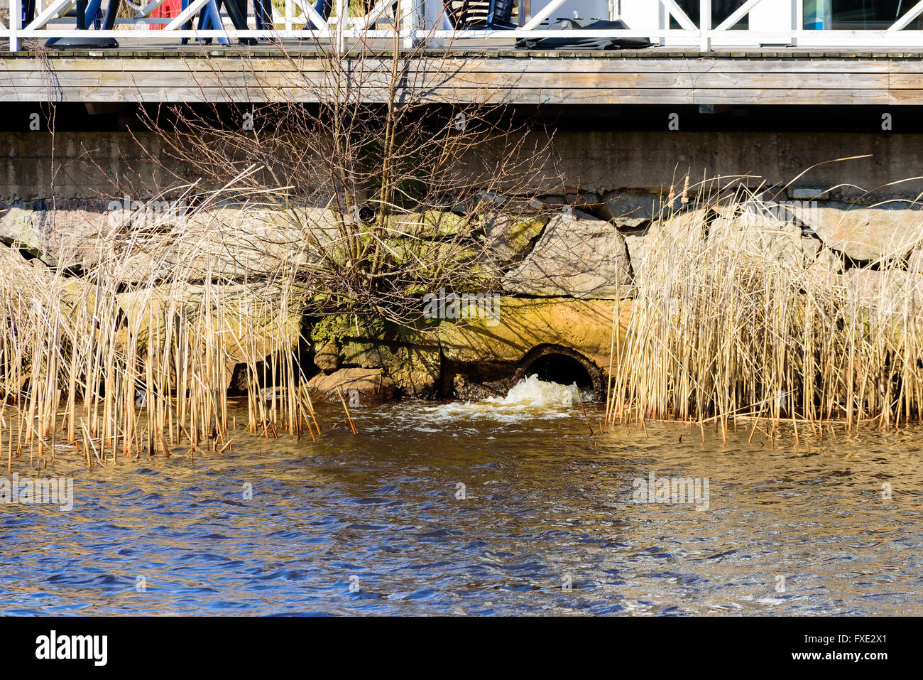 Salida de drenaje de tormentas en un río con bloques de piedra que rodea y parte de un espigón o puente por encima. Foto de stock