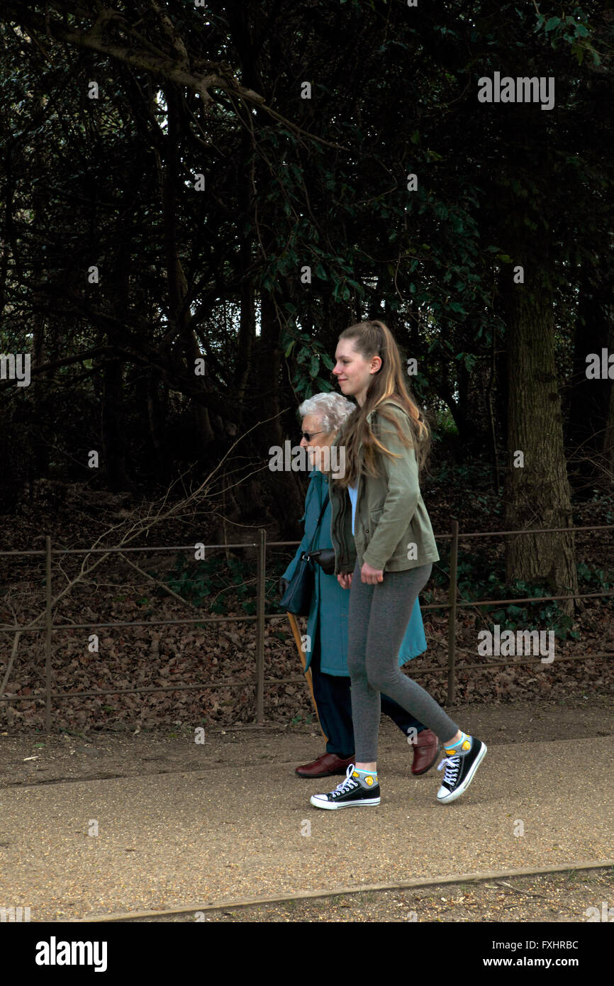 Una abuela y su nieta caminando en un parque. Con un octogenario cuidador adolescentes hepler. Foto de stock