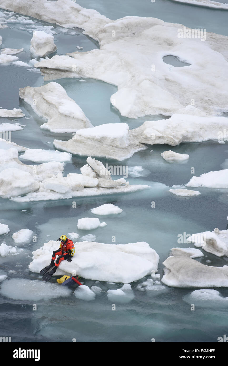 Un buceador de rescate de la Guardia Costera estadounidense descansa sobre un trozo de hielo marino en el Océano Ártico después de acercarse a una persona simulada en el agua durante la formación el 14 de julio de 2015 cerca de punto Oliktok, Alaska. La formación utiliza un maniquí térmico diseñado para tener el mismo calor firma de una persona en el agua. Foto de stock