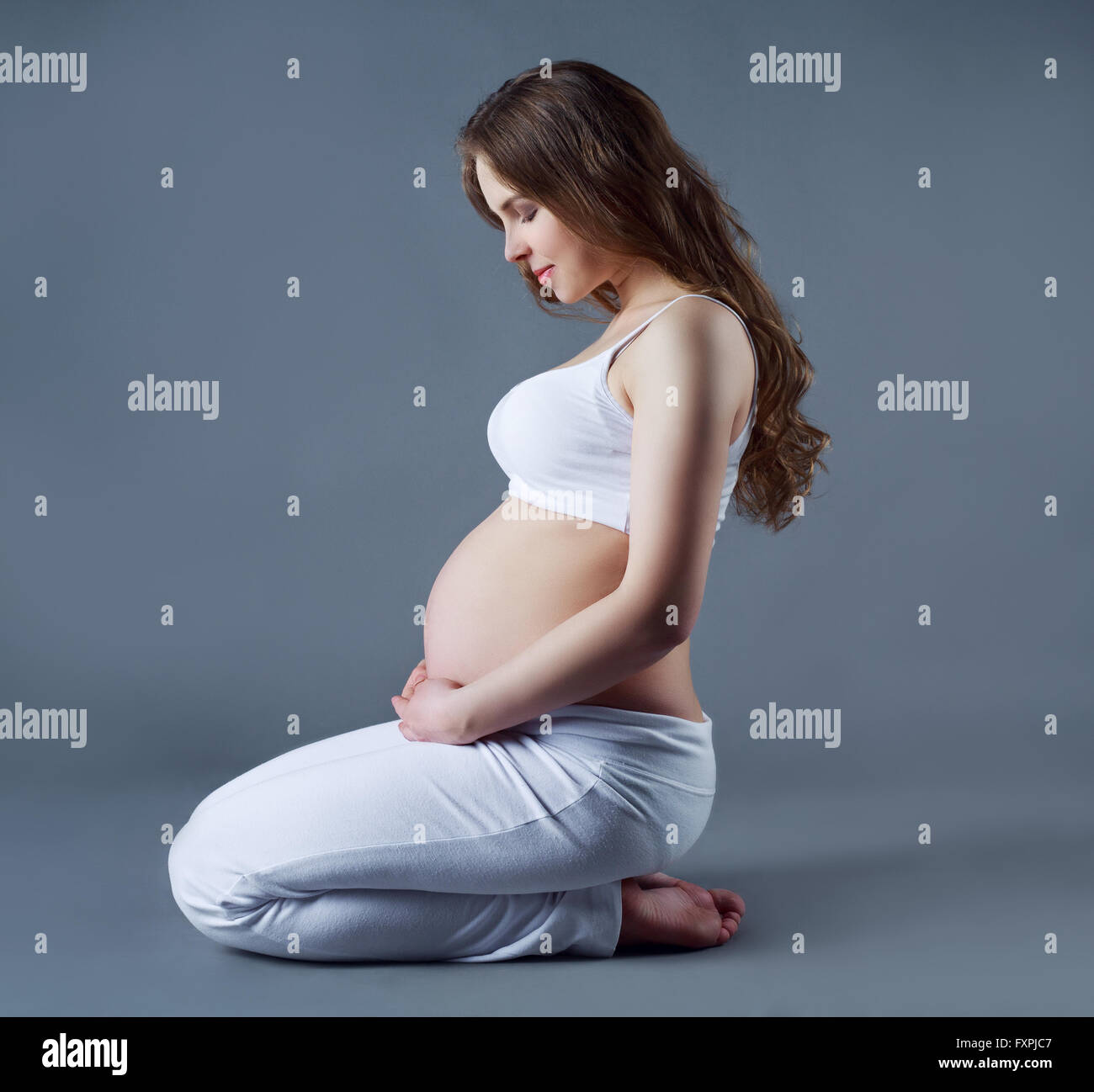 Perfil de una joven y bella mujer embarazada sentada en el suelo, contra el  gris de fondo studio Fotografía de stock - Alamy