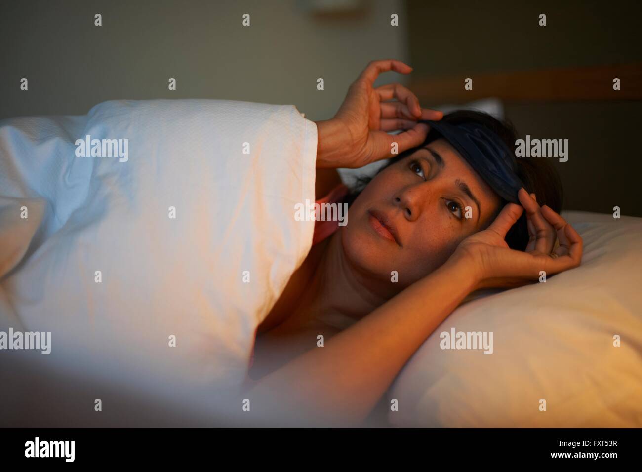 Mujer madura poniendo en máscara de ojo en la cama en la noche de hotel Foto de stock