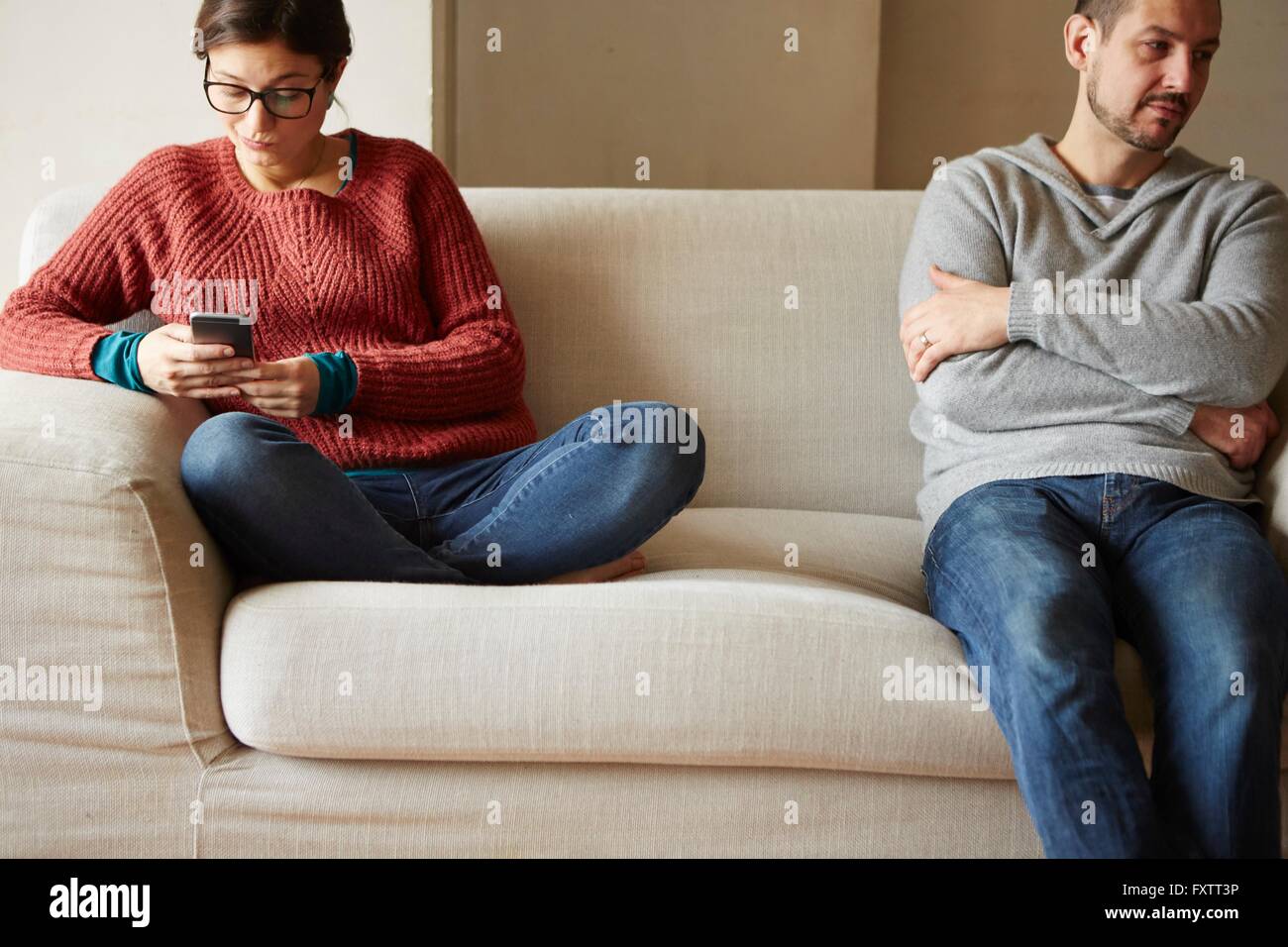 Refunfuñar hombre sentado en el sofá mientras lee novia mensaje de texto Foto de stock