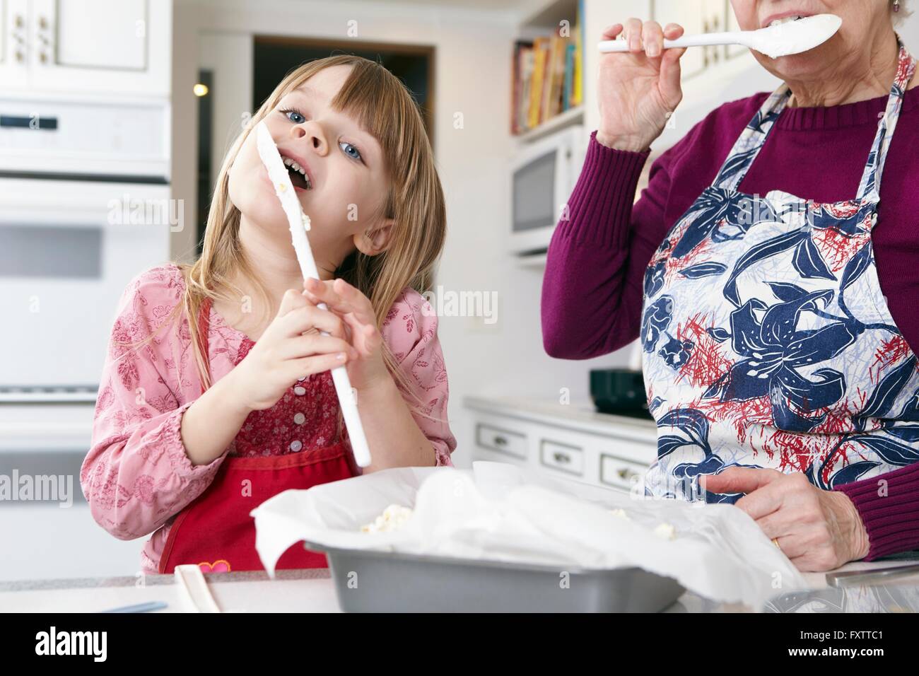 Niña y abuela lamer tarta de espátula en la cocina Foto de stock