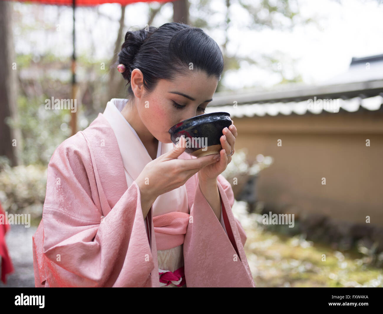 Mujer japonesa en kimono beber una taza de té verde en los jardines de Kinkaku-ji, un templo Budista Zen en Kyoto, Japón. Foto de stock