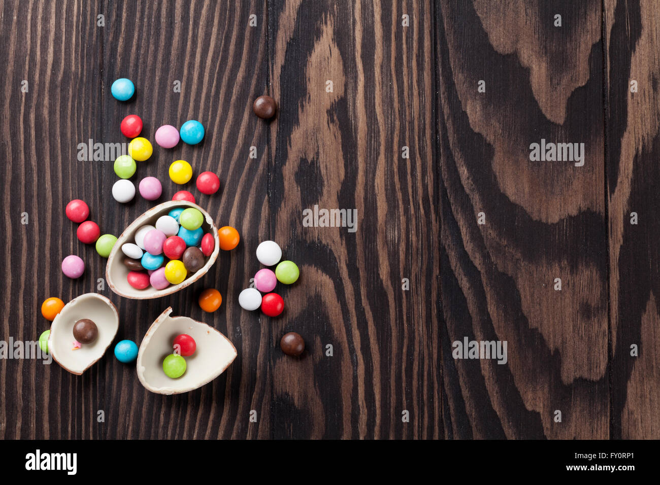 Caramelos de colores y huevo de chocolate sobre fondo de madera. Vista superior con espacio de copia Foto de stock