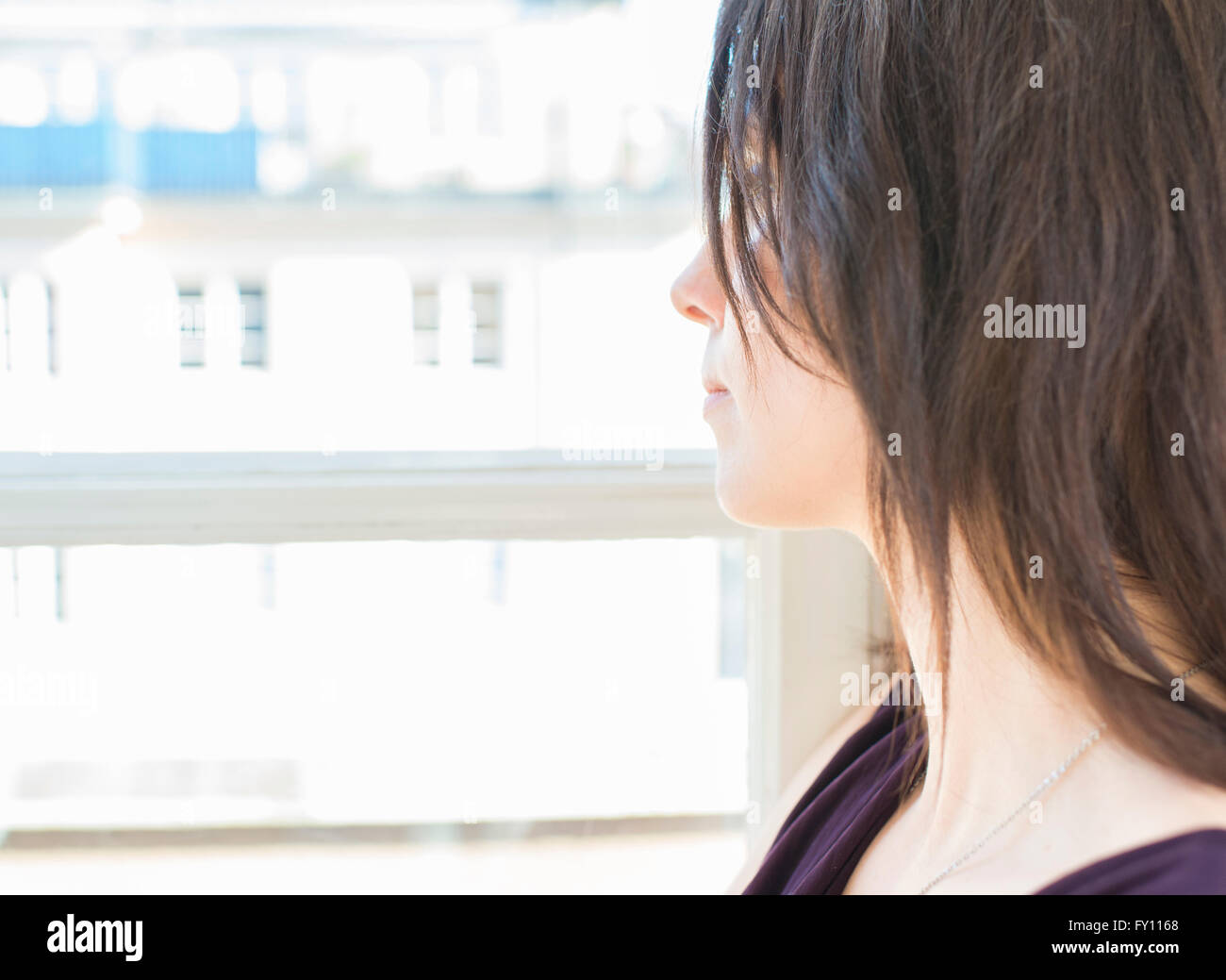Mujer de vestido negro de pie junto a una ventana, mirando a otro lado. Concepto de la soledad, la espera y la tristeza. Foto de stock