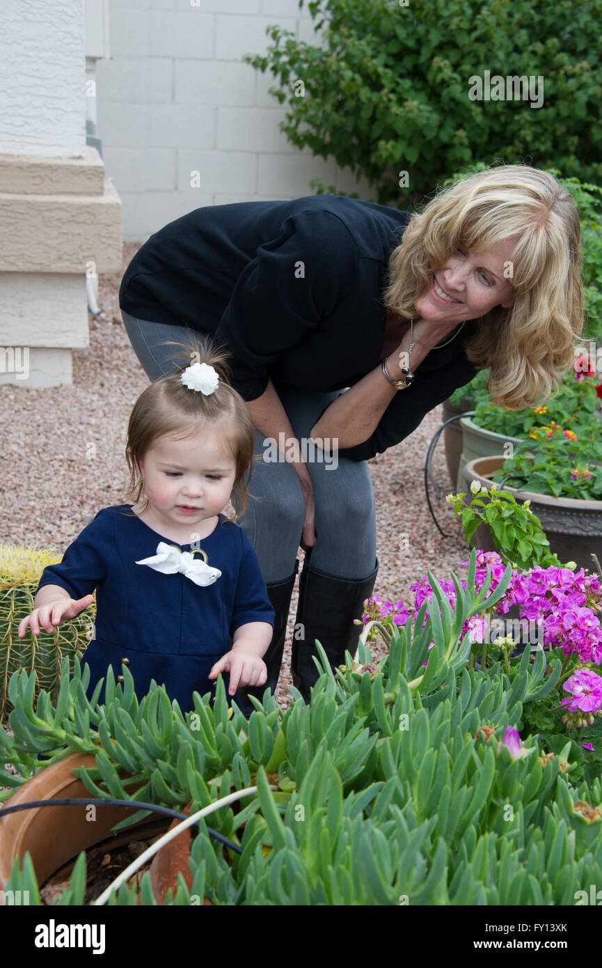 Una pequeña chica que llevaba un vestido azul jugando en un jardín con la abuela Foto de stock