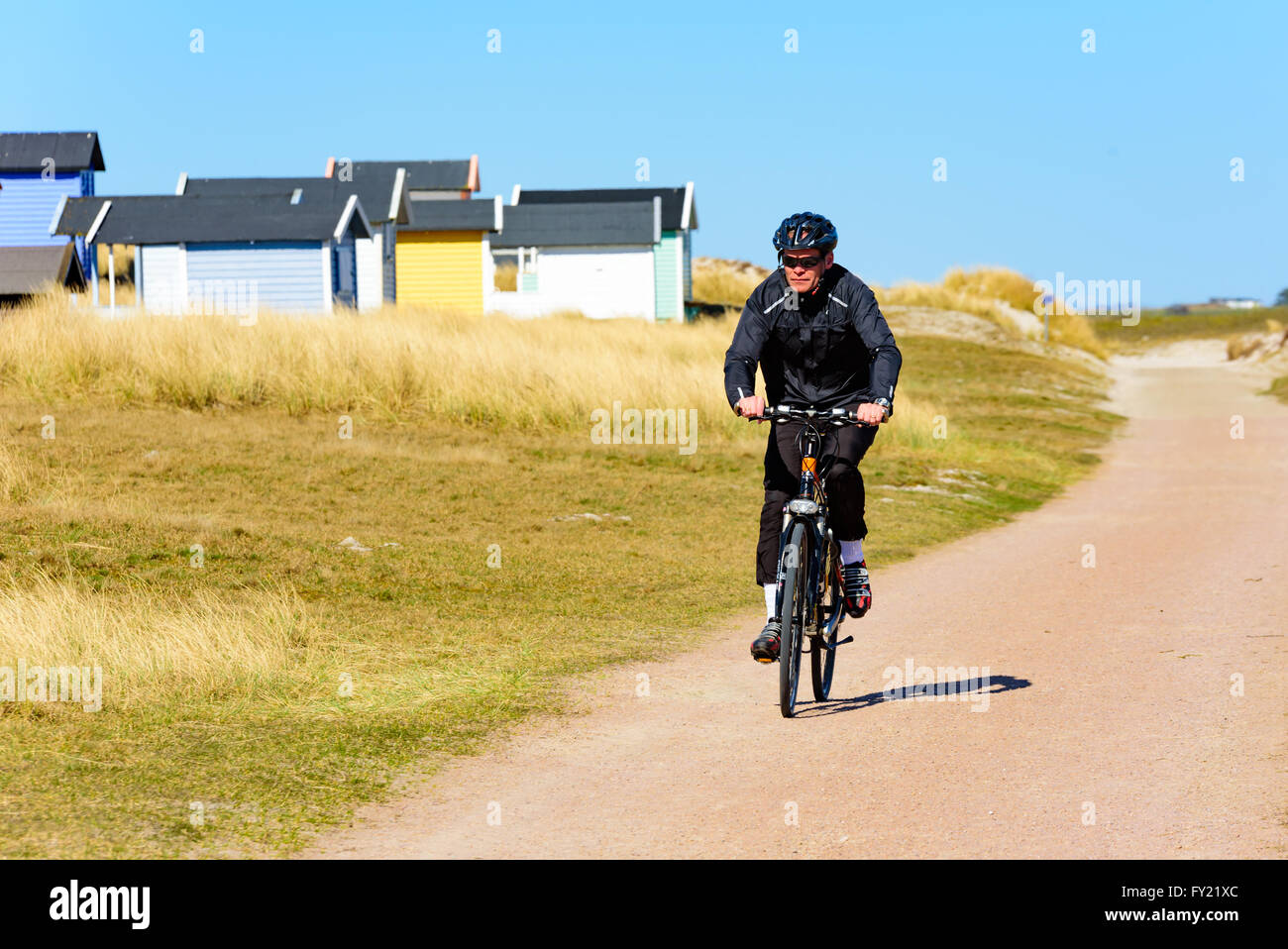 Skanor, Suecia - 11 de abril de 2016: Macho ciclista ejercicio a lo largo de una playa de arena camino o sendero, con una fila de casitas de baño ser Foto de stock