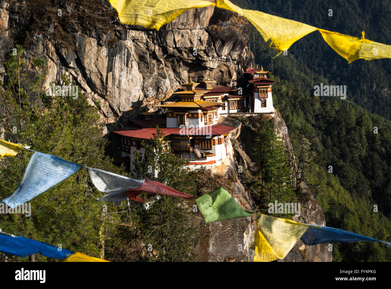 Vista entre banderas de oración a Tiger's Nest (Monasterio de Taktshang), encaramado sobre un acantilado cerca de Paro, Bhután Foto de stock
