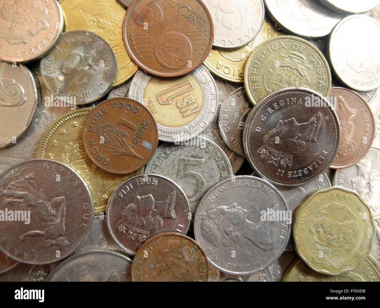 Montón de monedas extranjeras con fuerte fundido la luz procedente de la esquina superior derecha Foto de stock