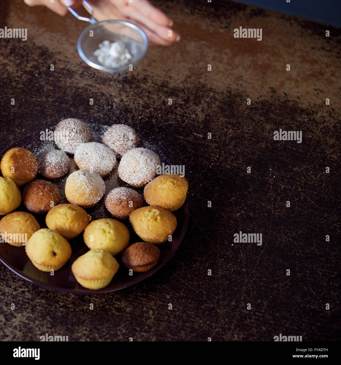 Mano de mujer espolvorear azúcar impalpable sobre muffins frescos. cerrar Foto de stock