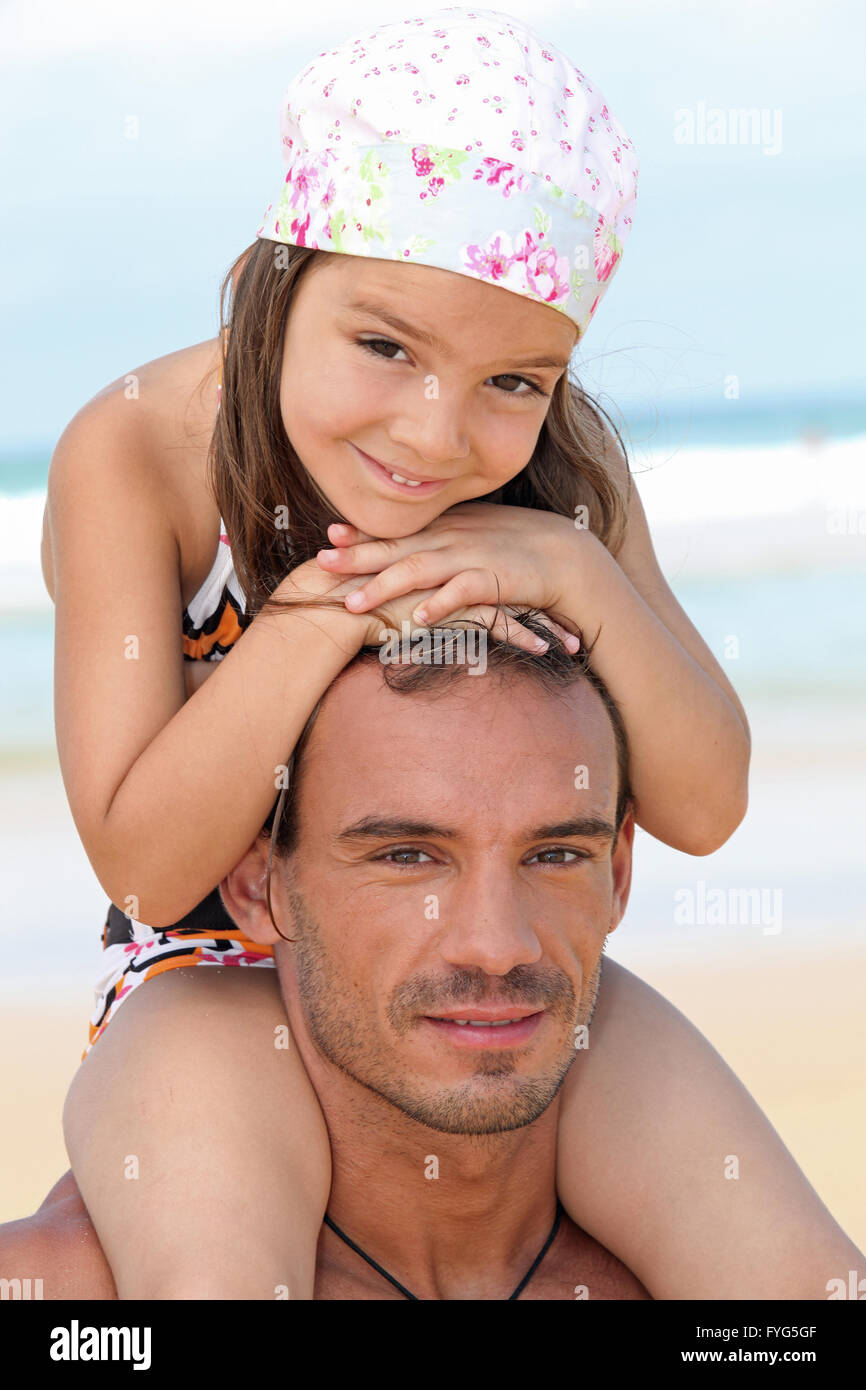 Niña sentada sobre los hombros del padre en la playa Foto de stock