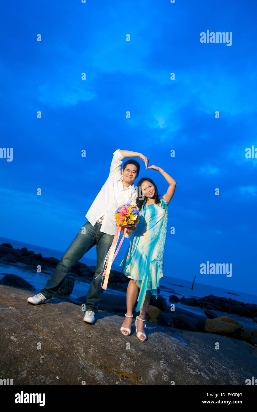 Las parejas jóvenes haciendo corazón firmar al atardecer en la playa Foto de stock