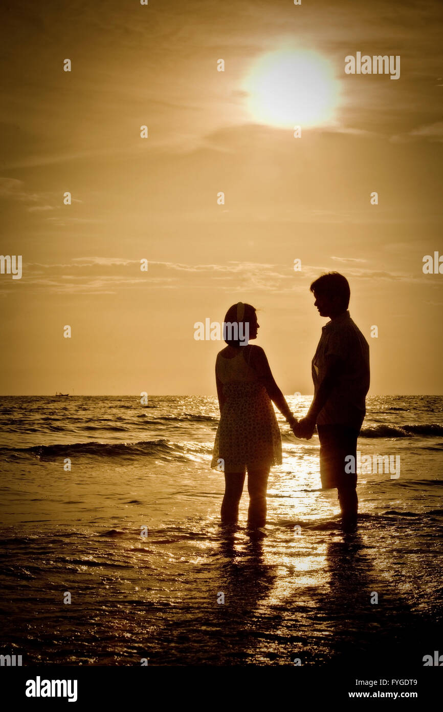 Romántica escena de parejas en la playa con puesta de sol Foto de stock