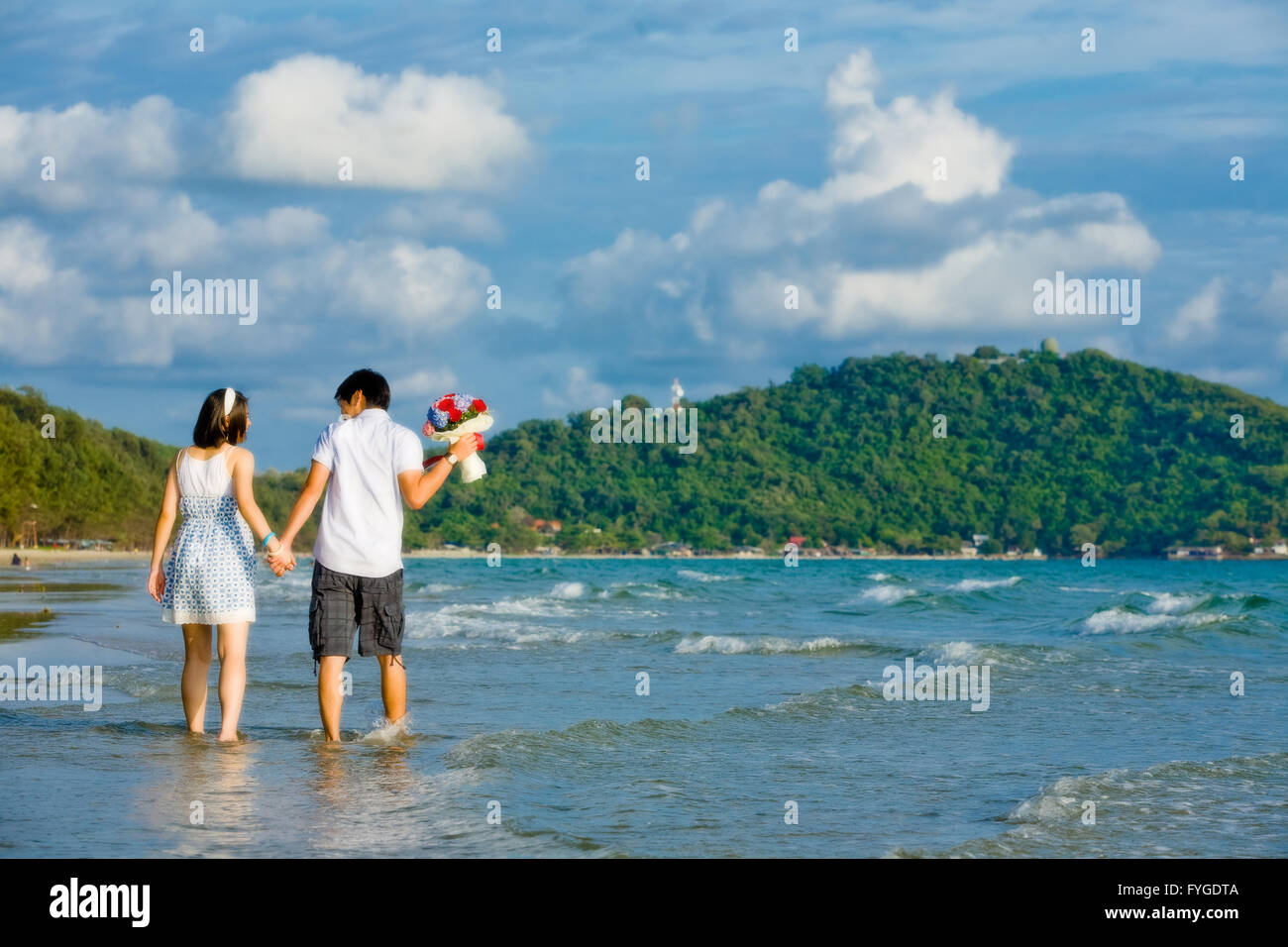 Dulce por parejas caminando de la mano a lo largo de la playa con una suave ondulación Foto de stock
