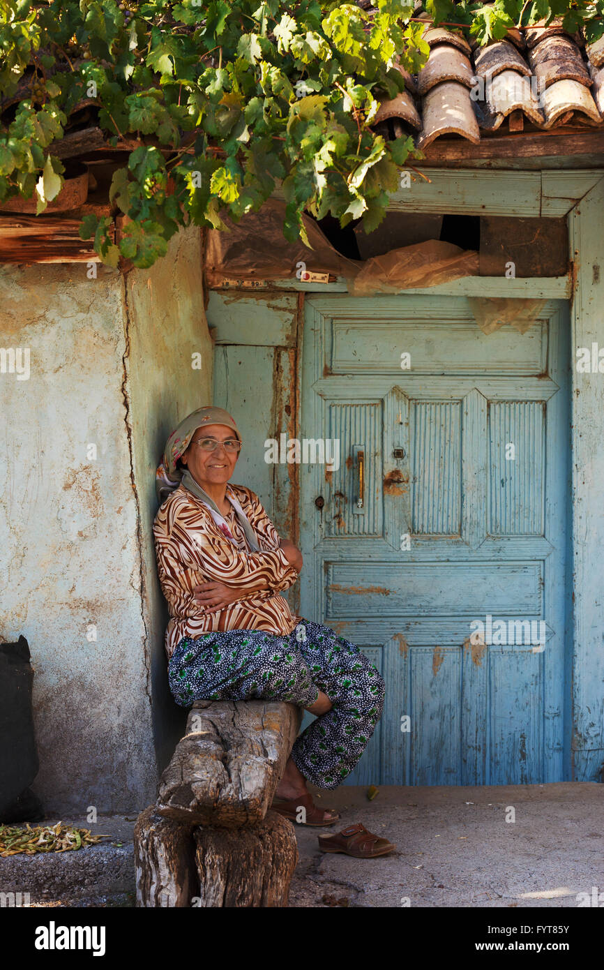 Mujer sentada delante de la entrada de la casa donde vive. Foto de stock
