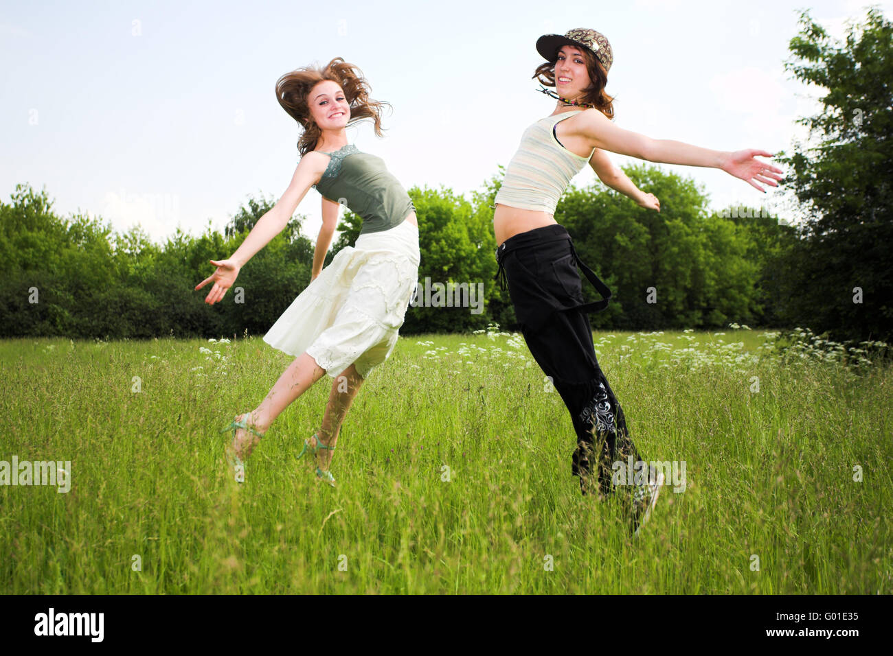 Dos niñas saltando sobre el cielo azul y el pasto verde Foto de stock