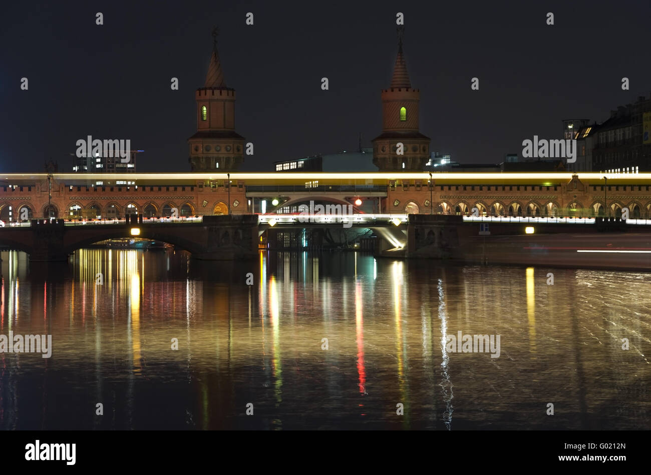 Berlín puente Oberbaumbrücke en la noche con el paso de un tren de metro y un barco Foto de stock
