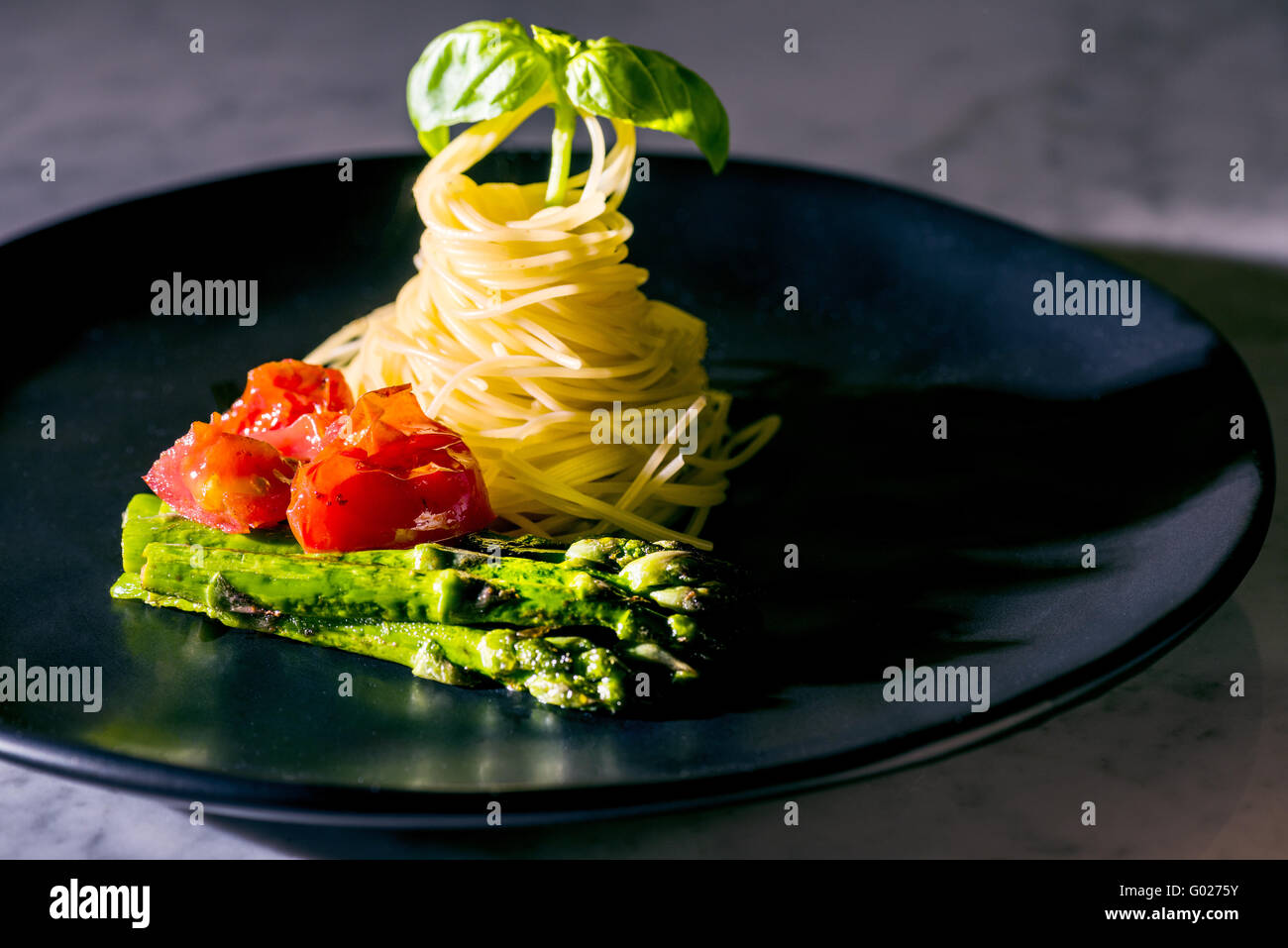 Fideos Fideos espaguetis tomates albahaca espárragos en placa negra verde rojo negro fine food italiano Italia elegante rápido kitch moderna Foto de stock