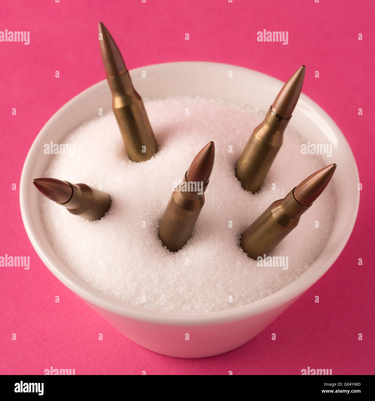 Cuenco blanco lleno de azúcar blanco y balas de rifle sobre fondo rosa Foto de stock