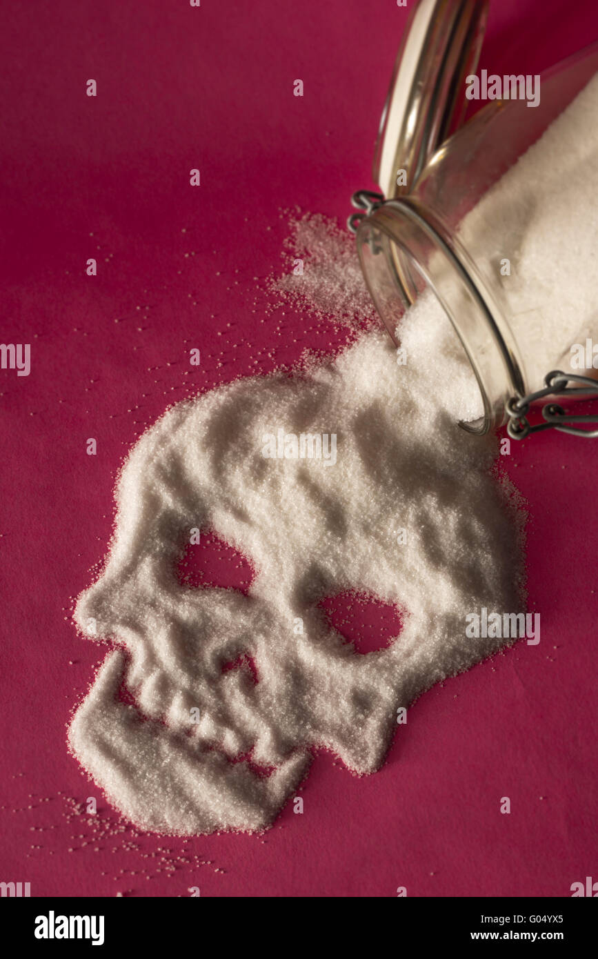 El azúcar blanco derramándose de un tarro de vidrio sobre fondo de color rosa y formando un cráneo cara Foto de stock
